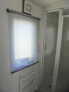 a bathroom with a shower and a window with blinds at Kingfisher : Seabreeze:- 6 Berth, Enclosed veranda, Close to site shop in Ingoldmells