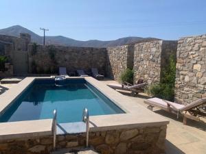 a swimming pool with chairs and a stone wall at Mandri B&B in Serifos Chora