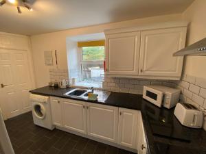 a kitchen with white cabinets and a sink and a microwave at Antur Cottage in Blaenau-Ffestiniog