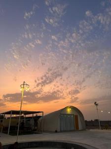 Desert Breeze Farm Resort في Al Ḩamrānīyah: خيمة بيضاء كبيرة في موقف للسيارات عند غروب الشمس