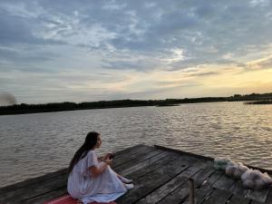 a woman sitting on a dock on a lake at Mechrey Tonle Camp Site in Siem Reap