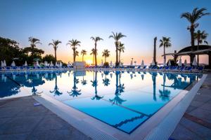 a pool with chairs and palm trees and the sunset at MIRADA DEL MAR HOTEL in Antalya