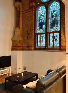 Magical Church Conversion in Watford في واتفورد: غرفة معيشة مع أريكة جلدية ونوافذ زجاجية ملطخة