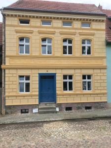 un bâtiment jaune avec une porte bleue devant lui dans l'établissement Martinsgarten, à Angermünde