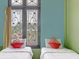 twee bedden met rode kussens voor een raam bij OYO 92872 Swakarya Guest House in Parit
