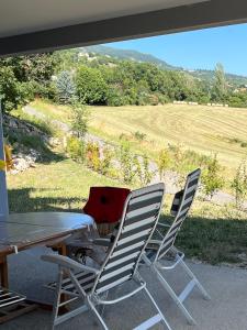 trzy krzesła i stół na werandzie z widokiem na pole w obiekcie Lac et Montagne w mieście Chorges