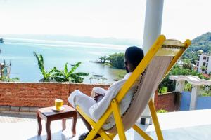 a man sitting in a chair looking out at the water at Green Safaris Apartment in Rubavu