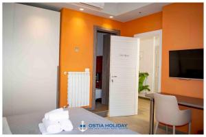 Habitación con pared de color naranja, mesa y TV. en Ostia Holiday Sunset, en Lido di Ostia