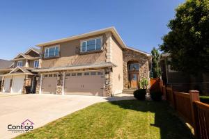 a house with two garage doors and a fence at Luxury Retreat, Sleeps 12, AC, Patio, 5 min to YQL in Lethbridge