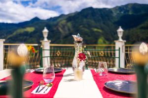 a table with a red table cloth with plates and wine glasses at B&B Das Land-Palais - PRIVATE Mountain Hideaway in Selva dei Molini