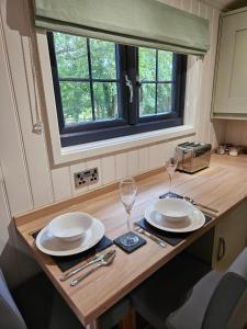 una mesa con dos platos y copas de vino. en Woodland Shepherds Hut - 'Saga', en Caernarfon