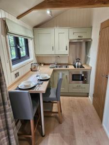 una pequeña cocina con mesa, sillas y fregadero en Woodland Shepherds Hut - 'Saga' en Caernarfon