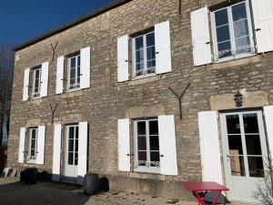 un edificio de ladrillo con ventanas blancas con contraventanas y una mesa roja en La Flavignienne en Flavigny-sur-Ozerain