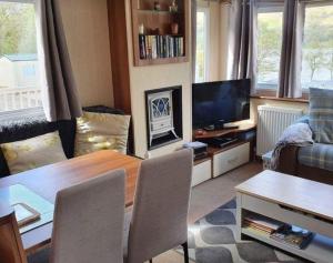 sala de estar con mesa, sofá y TV en Loch Earn Holiday Home, en St Fillans