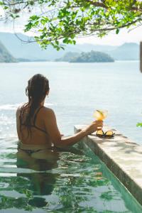 una mujer sentada en una piscina junto a un cuerpo de agua en Casa Luz, en Paraty