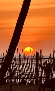 a sunset on the beach with the sun behind a fence at CocoVilla Boutique Resort in Beruwala