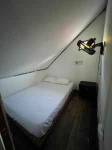 Dormitorio pequeño con cama blanca y lámpara en Hostal Kaia, en Santa Marta