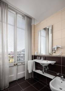 ein Bad mit einem Waschbecken, einem Spiegel und einem Fenster in der Unterkunft Hôtel des Alpes in Nyon