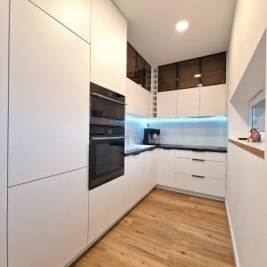 a kitchen with white cabinets and wood floors at APARTMAN LORINČIK KOSICE in Košice