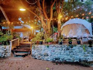 a patio with a stone wall and a tree and a tent at Beach Glamping Dome Dauin Modern Style in Dauin