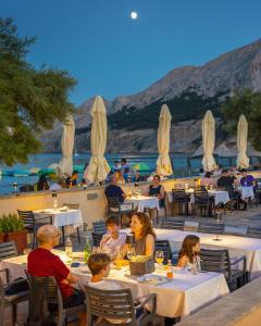 a group of people sitting at tables at a restaurant at Hotel Dobrovit in Baška
