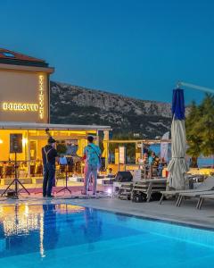 two people standing next to a swimming pool at Hotel Dobrovit in Baška