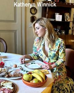 una mujer sentada en una mesa con un tazón de fruta en Residenza d'Epoca Palazzo Borghesi, en Siena