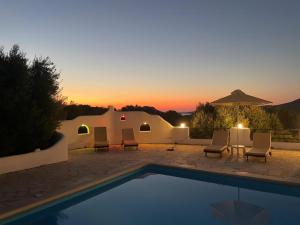 a pool with chairs and a sunset in the background at Cavo Plako Villas in Palekastron