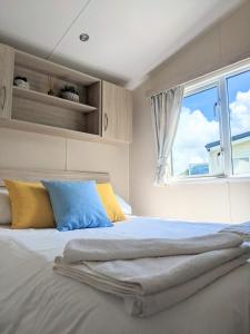 a bed with yellow and blue pillows and a window at Large 4 person Couples and Family Caravan in Newquay Bay Resort in Newquay
