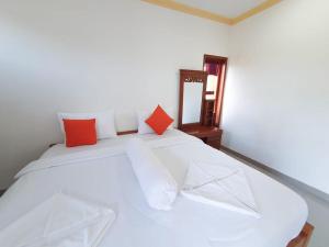 ein weißes Bett mit orangefarbenen und weißen Kissen darauf in der Unterkunft Batur Happy House in Kintamani