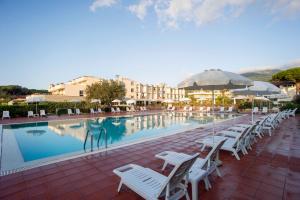 uma piscina com cadeiras brancas e guarda-sóis em Hotel Select em Marina di Campo