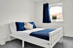 a white bed with blue pillows and a window at Serviced accomodation - For Families or Corporate in London