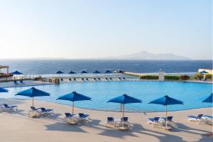 a large pool with blue umbrellas and chairs and the ocean at Cleopatra Luxury Resort Sharm El Sheikh in Sharm El Sheikh