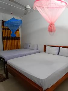 two beds in a room with pink and blue curtains at Pranu House in Nilaveli