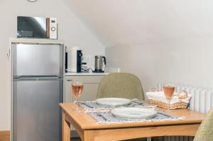 Exquisite Coach House Near Silverstone & Stowe في باكنغهام: مطبخ مع طاولة مع كؤوس للنبيذ وثلاجة