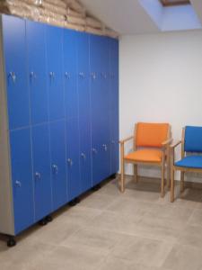 a row of blue lockers in a room with two chairs at Albergue de Maella in Maella