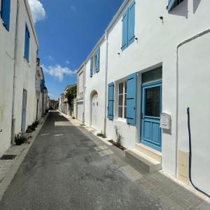 an empty street with white buildings with blue windows at L'OCEAN a Oleron in Le Château-dʼOléron