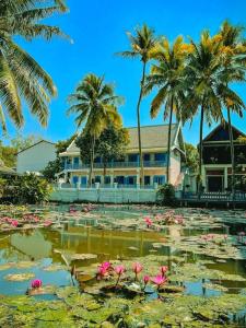 a house with palm trees and a pond with pink flowers at Sadakham Hotel in Luang Prabang