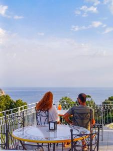 Ein Mann und eine Frau sitzen an einem Tisch und sehen auf den Ozean. in der Unterkunft RIAMA AGRIRESORT in Neapel