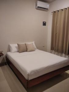 uma cama com lençóis brancos e almofadas num quarto em Apartamento em Bacalar