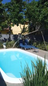 a swimming pool with two lawn chairs and trees at CASA TROPICANA - ITAÚNAS Centro in Itaúnas