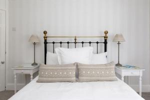 1 cama con almohadas blancas y 2 mesas con lámparas en The Kept Cottage, en Hassocks