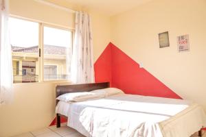a bedroom with a bed with a red wall at Apartamento a 50m da praia da Enseada. in São Francisco do Sul