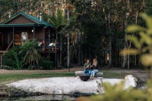 two people sitting on a bench in front of a house at Lake Weyba Cottages Noosa in Peregian Beach