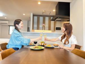Dos mujeres sentadas en una mesa con copas de vino en Garland Court Usami Private Hot Spring Condominium Hotel, en Ito