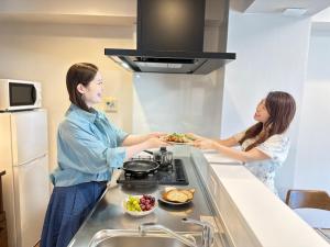 Garland Court Usami Private Hot Spring Condominium Hotel في إيتو: كانتا امرأتان واقفتان في مطبخ لإعداد الطعام