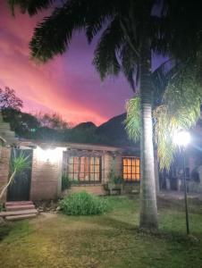 a house with a palm tree in front of a sunset at El quincho in Las Padercitas