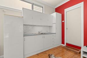 a kitchen with white cabinets and a red wall at Kingston Gardens by Experience Jervis Bay in Huskisson