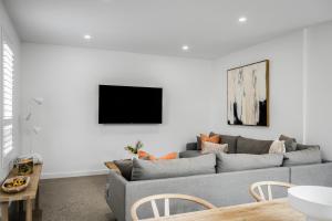 ein Wohnzimmer mit einem grauen Sofa und einem TV an der Wand in der Unterkunft Vale 194 - Newly built in McLaren Vale - 5 holiday homes with king size beds in McLaren Vale