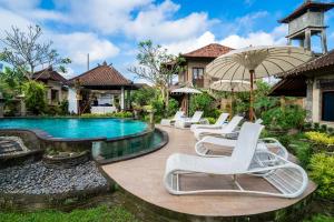 a pool with white lounge chairs and an umbrella at Capung Cottages in Ubud